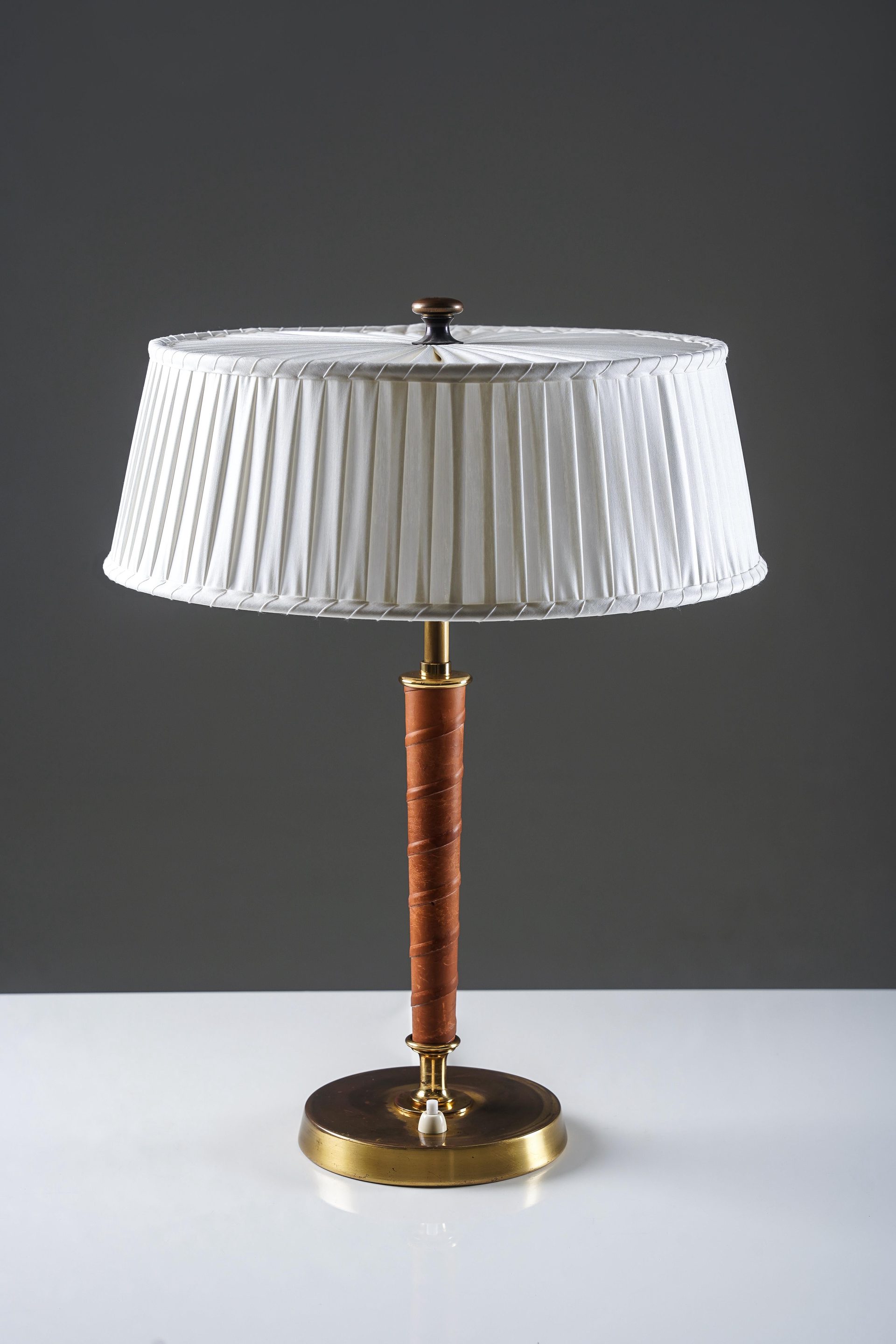 Elegant table lamp model 32926 produced by Nordiska Kompaniet in the 1940s. The lamp features a refined combination of brass and a leather-wrapped stem, adding both texture and warmth to the design. The circular base in brass provides a stable and