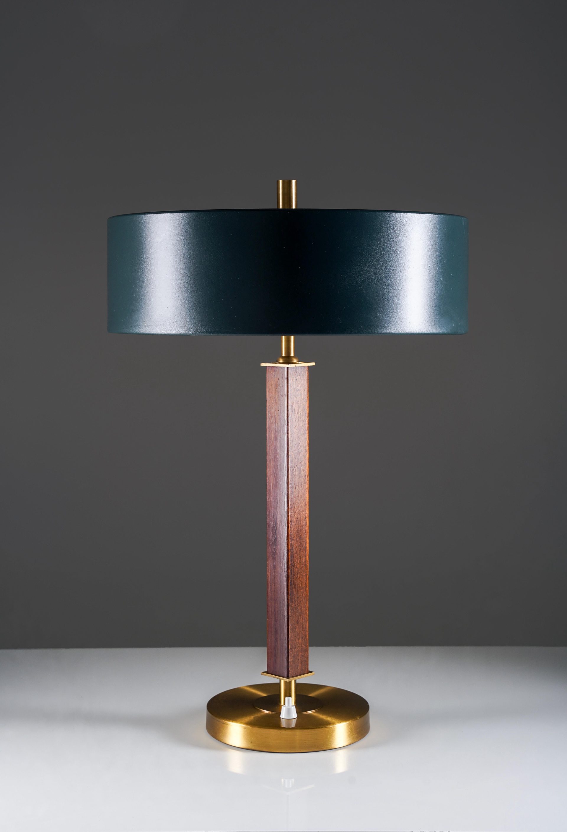 A refined Swedish table lamp from the 1960s, produced by Einar Bäckströms Metallvarufabrik. The design combines a solid brass base with a slender wooden stem, creating a warm contrast between metal and natural material.
The wide, cylindrical metal